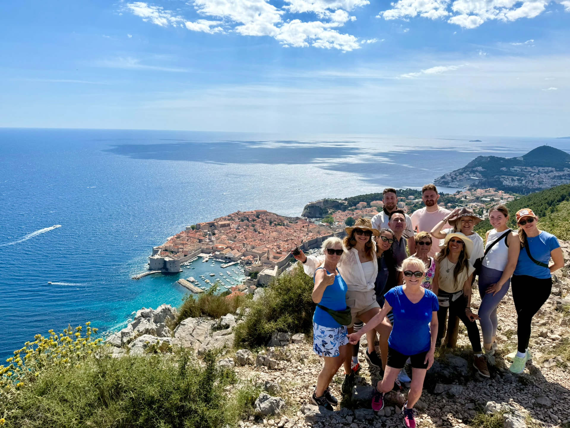 A smiling group of guests on a sunny ridge above Dubrovnik, with the Old Town and the Adriatic behind them